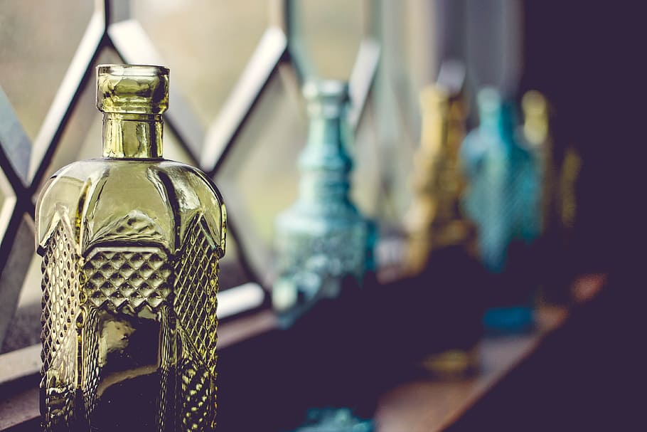 shallow focus photography of yellow glass bottle beside window, five assorted-color glass bottles on brown surface