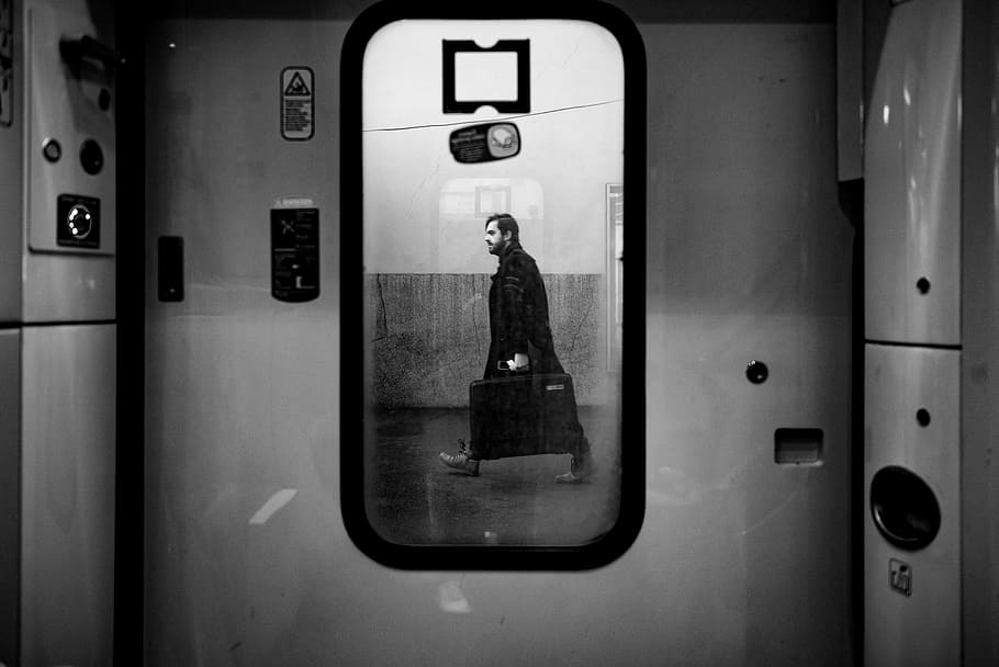 man walking outside train door in grayscale photo, grayscale photo of window with the view of man carrying luggage bag HD wallpaper