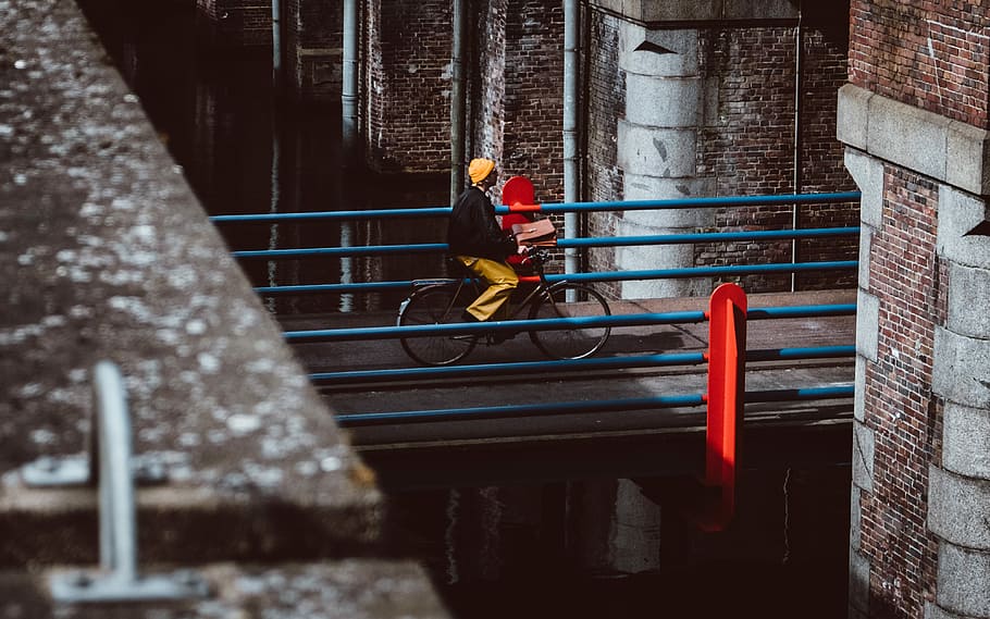 man riding bicycle on gray concrete bridge during daytime, woman riding bike along concrete bridge during day