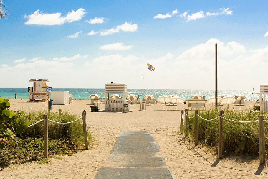 gray pathway leading to parasol, lifeguard house, and sea a daytime, white patio umbrellas on sand beside beach HD wallpaper
