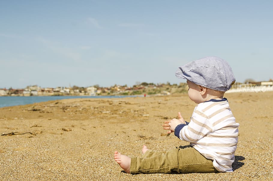 baby in white and brown striped long-sleeved shirt and pants outfit sitting on brown sand at daytime HD wallpaper