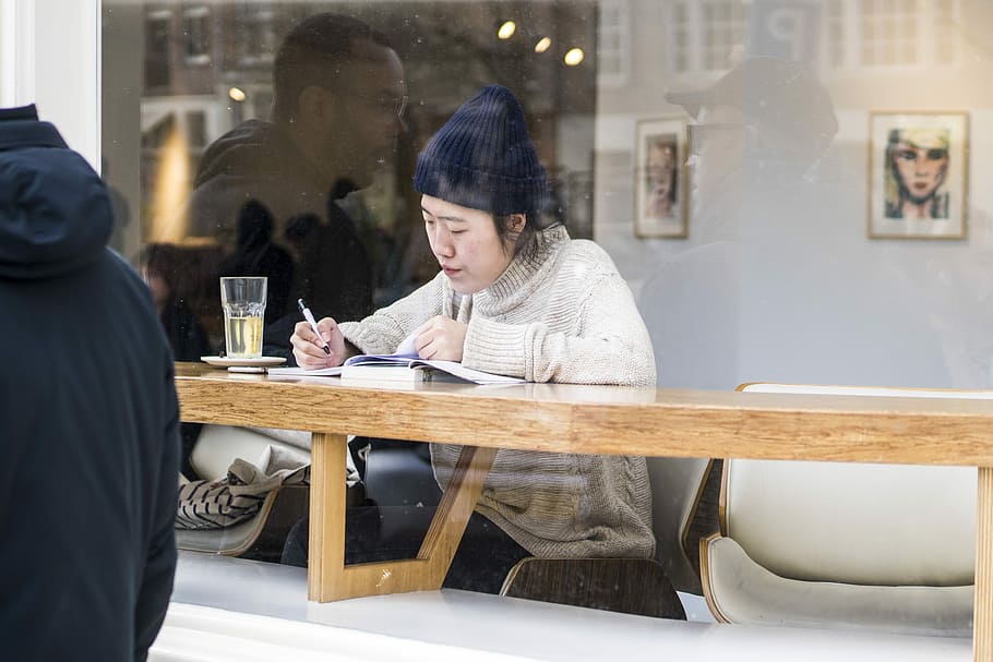 woman sitting in front of wooden table, woman writing on brown wooden table HD wallpaper