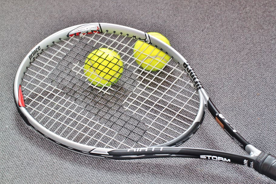black and white Prince Strom lawn tennis racket and two green tennis balls on gray surface
