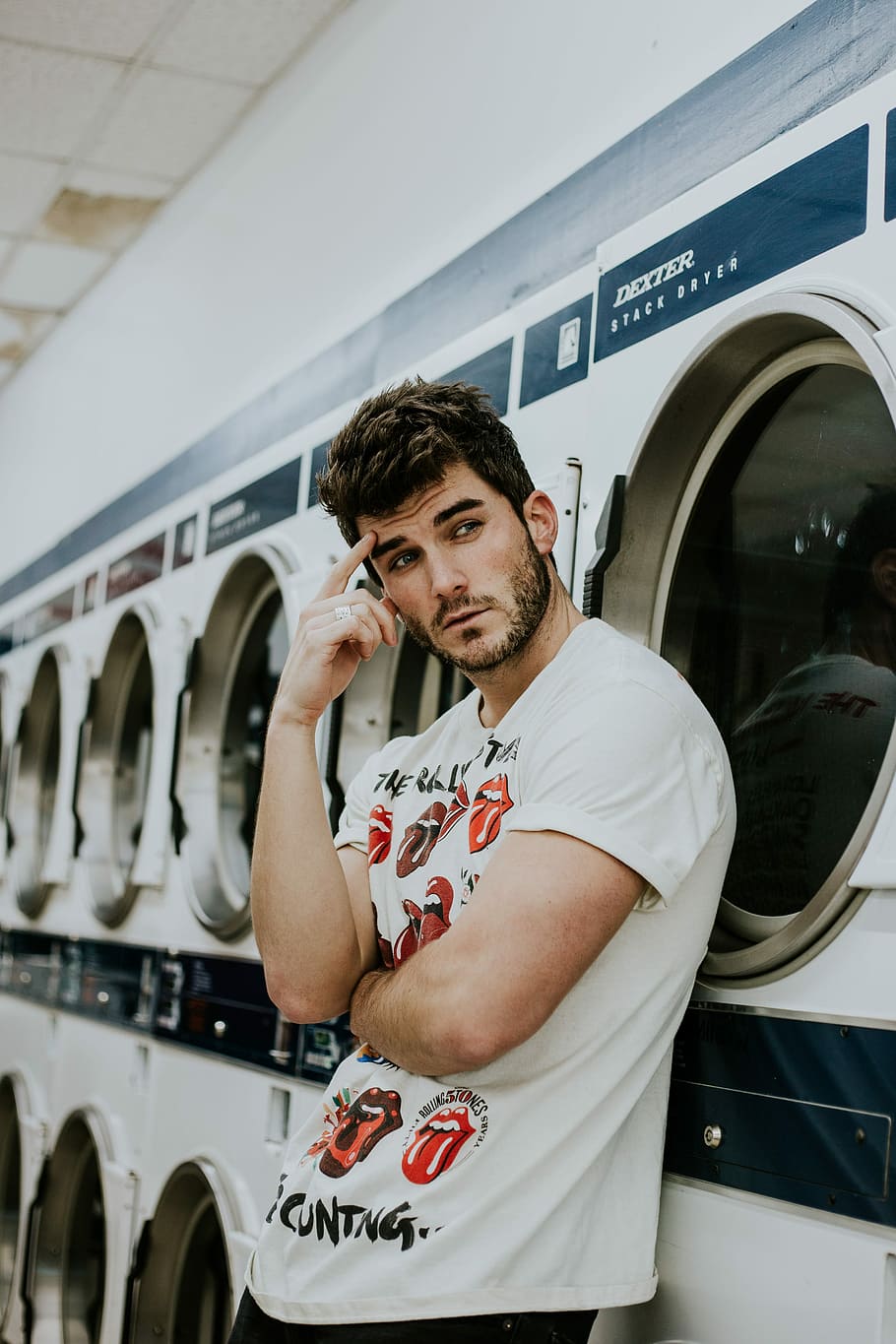 man leaning in front of clothes washer and dryer, laundry mat