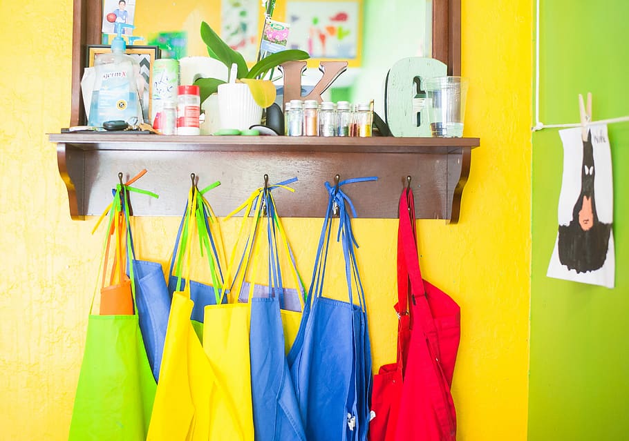 assorted-color bag lot hanging on brown wooden wall rack, assorted-color aprons hanging on pegs on wall