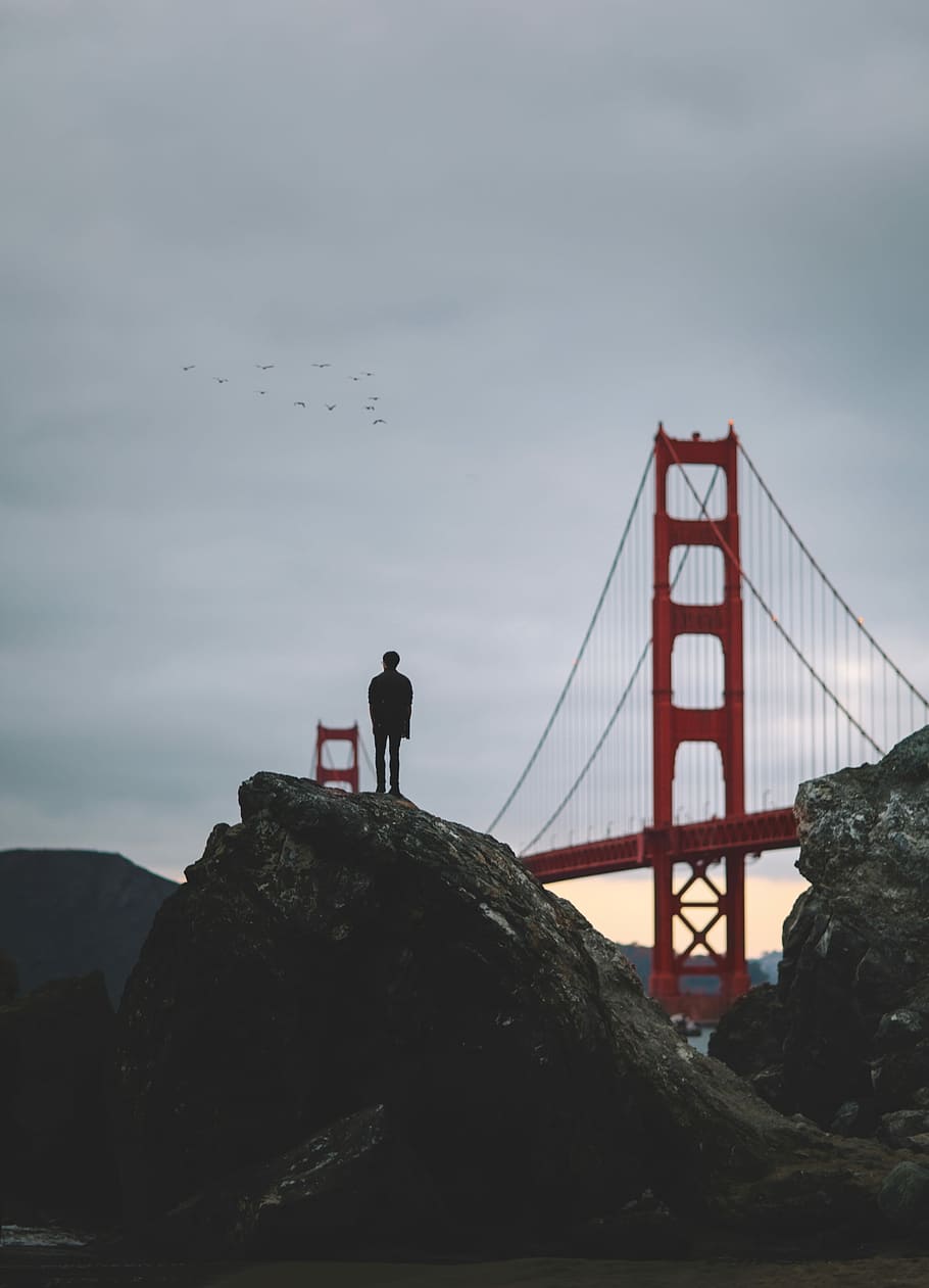 silhouette photo of a man on rock formation facing London Bridge during daytime HD wallpaper