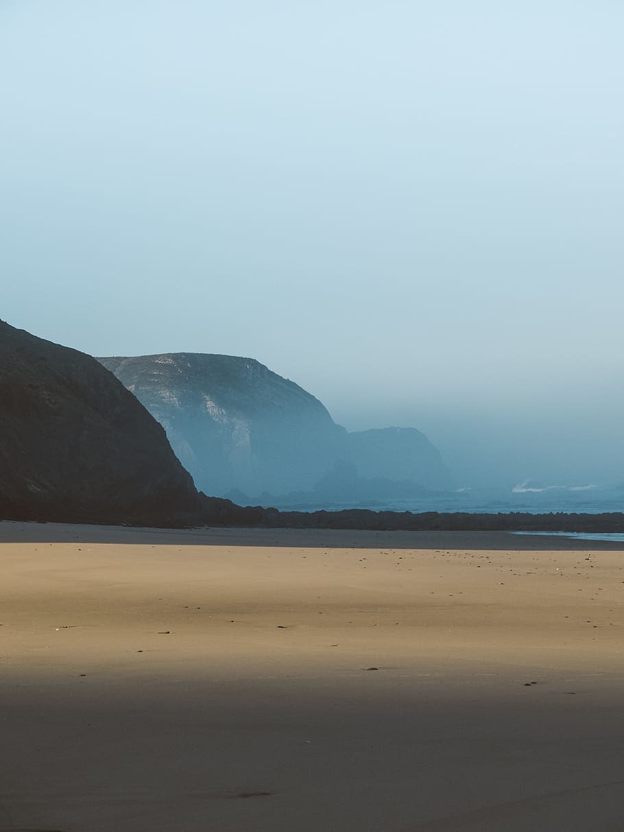 mountain covered with smoke beside body of water at daytime, landscape photography of shore near cliff at daytime HD wallpaper