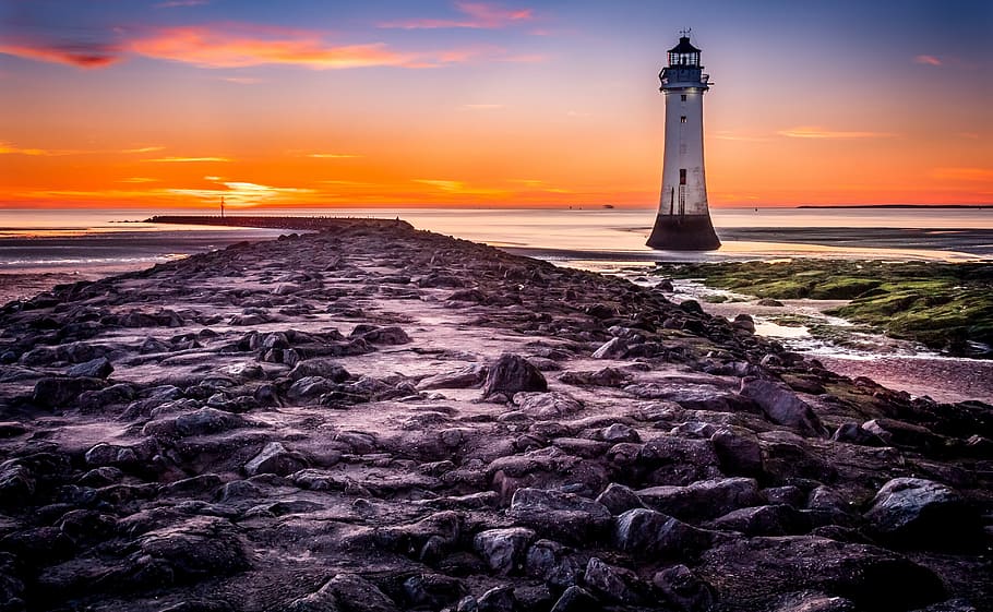 photo of lighthouse surrounding body of water during golden hour HD wallpaper