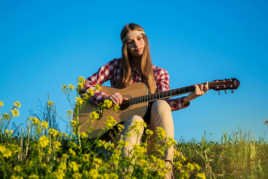 woman in red and white gingham long sleeve top sitting while playing brown acoustic guitar surrounded by yellow petaled flowers during daytime, HD wallpaper