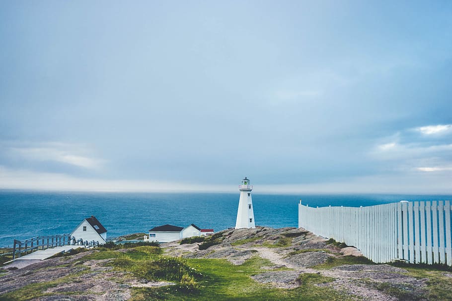 lighthouse on cliff near fence and house, white lighthouse and two houses inside the fence with wide body of water in distance HD wallpaper
