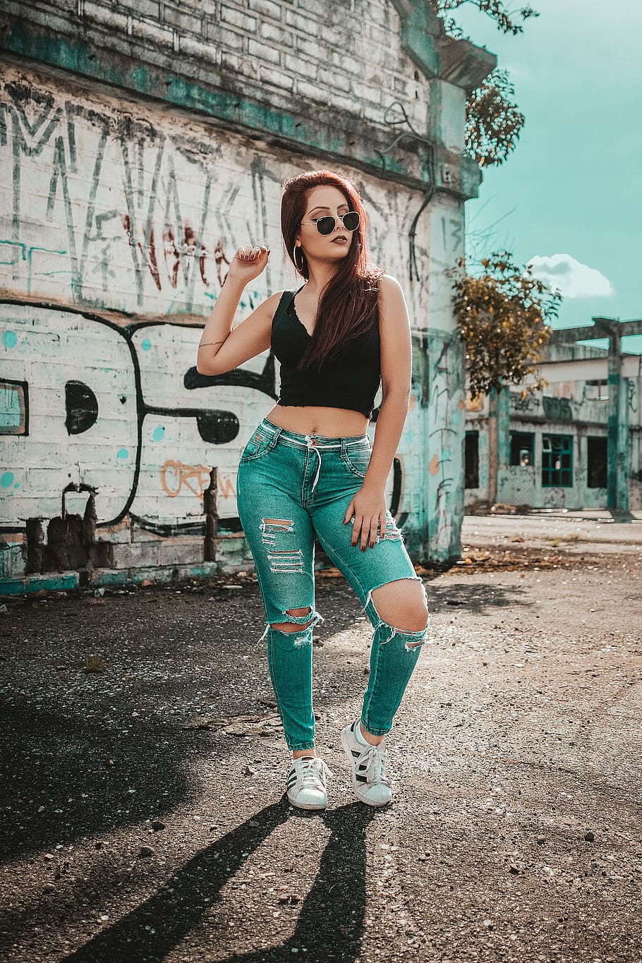 woman wearing black V-neck sleeveless top and distressed blue denim pants outfit while taking photo, woman standing near concrete building during daytime, HD wallpaper