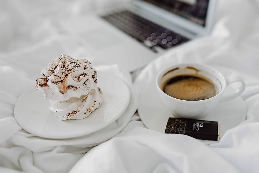 Woman working on a laptop while enjoying a breakfast coffee and chocolate in bed