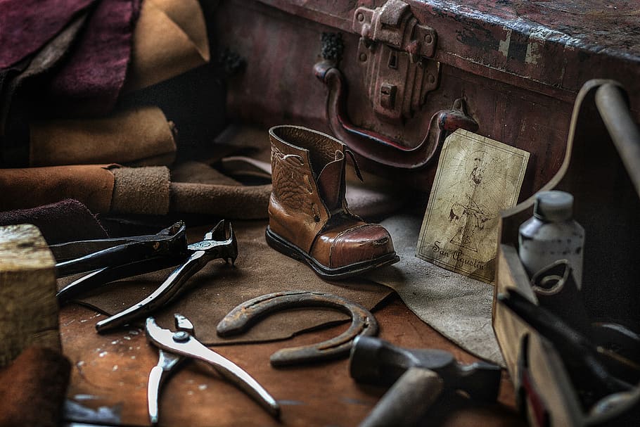assorted hand tools with unpaired brown work boot, brown leather boot and gray pliers beside brown case