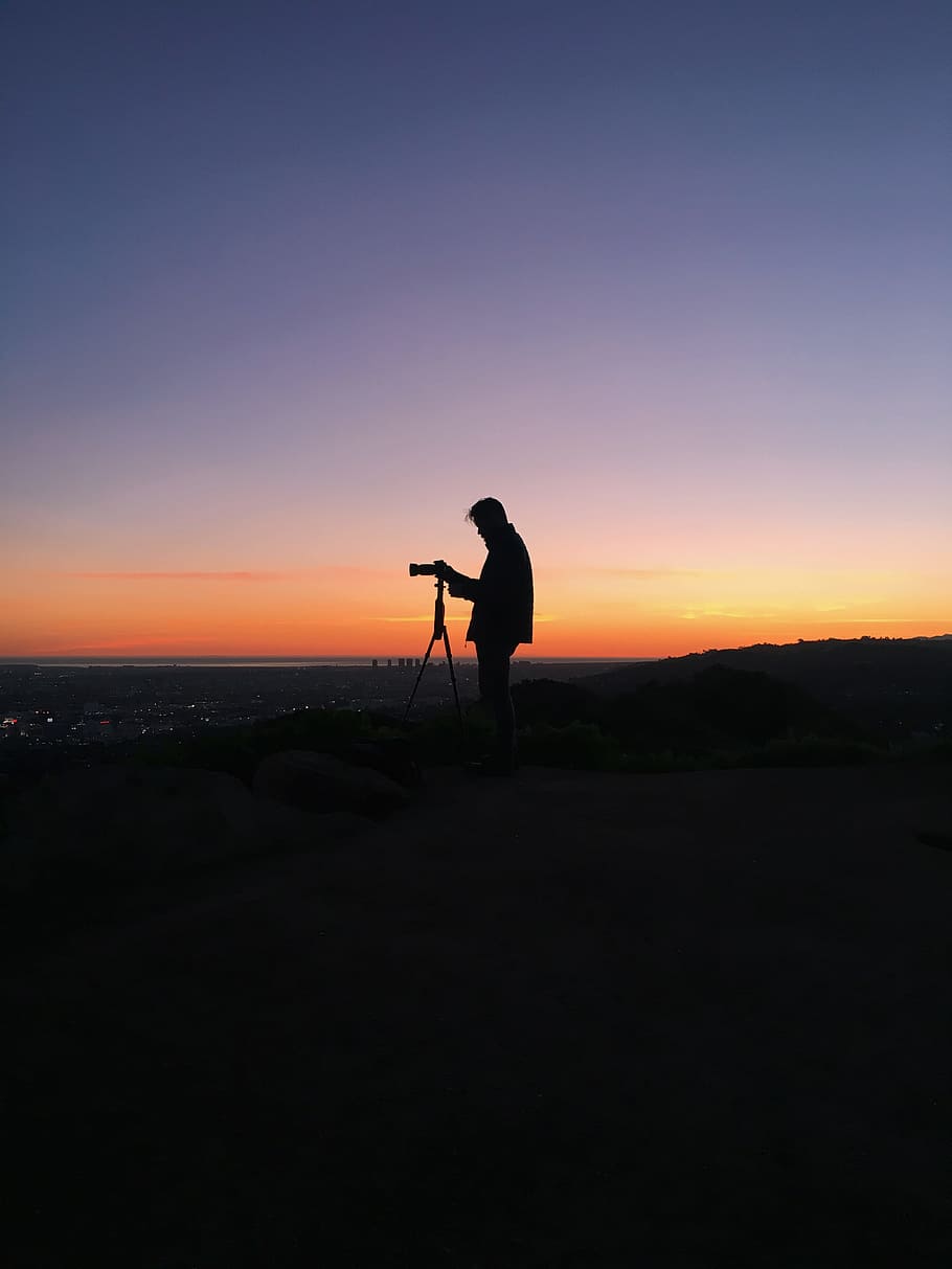 silhouette of man in front of DSLR camera during golden hour, silhouette photo of a man standing at the peak of the mountain using DSLR camera HD wallpaper