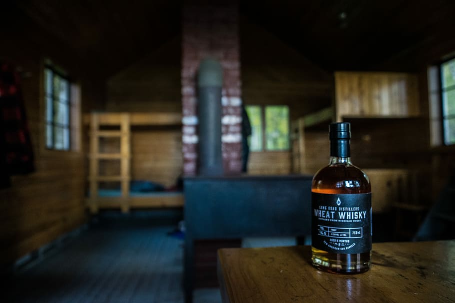 shallow focus photography of Wheat Whisky bottle on brown wooden table inside house, black Wheat Whisky bottle on brown wooden table HD wallpaper