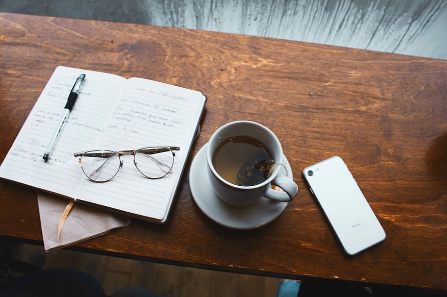 cup of tea on saucer beside white iPhone, white ceramic mug with tea on white ceramic saucer on brown wooden table HD wallpaper
