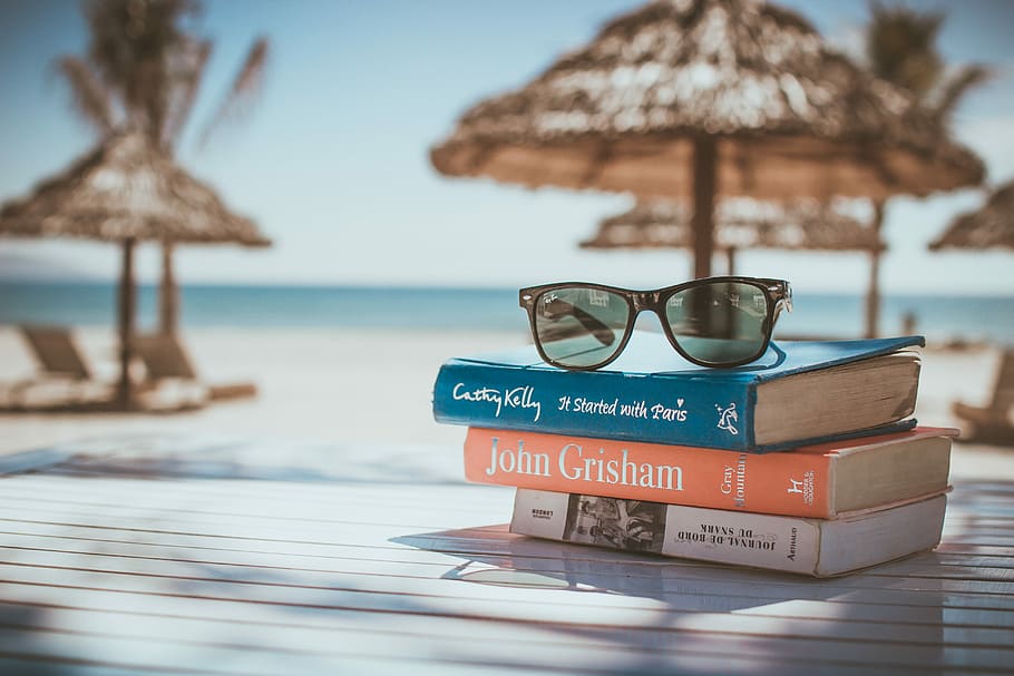 black framed Ray-Ban Wayfarer sunglasses on top of book, selective focus photography of three piled assorted-title reading books with brown sunglasses on top