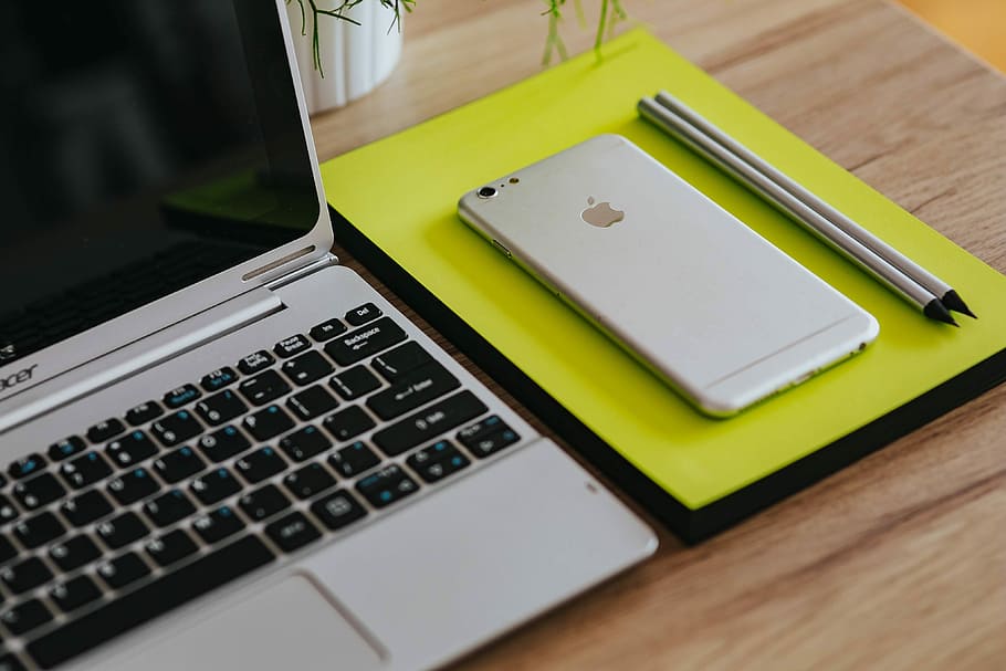 Silver Acer laptop, a white Apple iPhone and a notepad on a wooden desk HD wallpaper