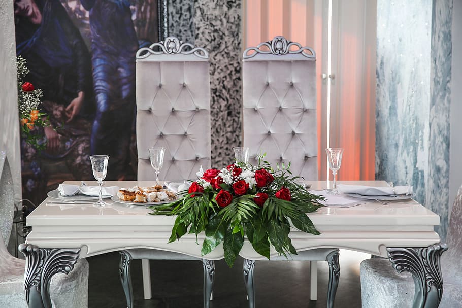 red roses arrangement on white wooden table with two tufted white chairs and wine glasses HD wallpaper