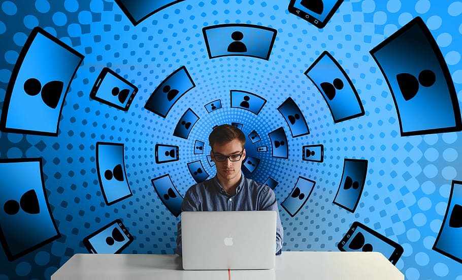 man sitting on table with blue background while using laptop