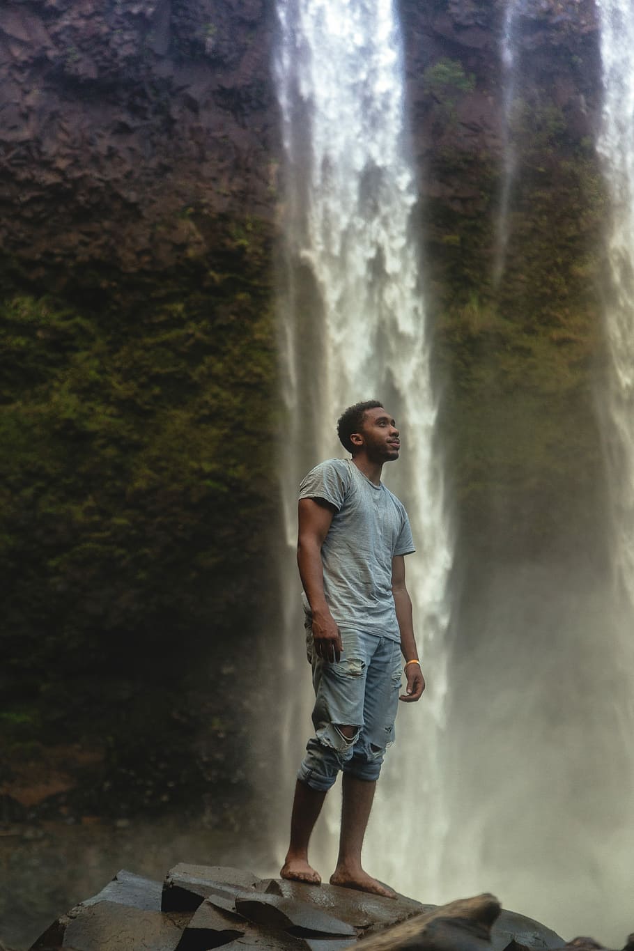 man standing near waterfall wearing gray crew-neck t-shirt and blue distressed denim pants, man standing near waterfalls HD wallpaper