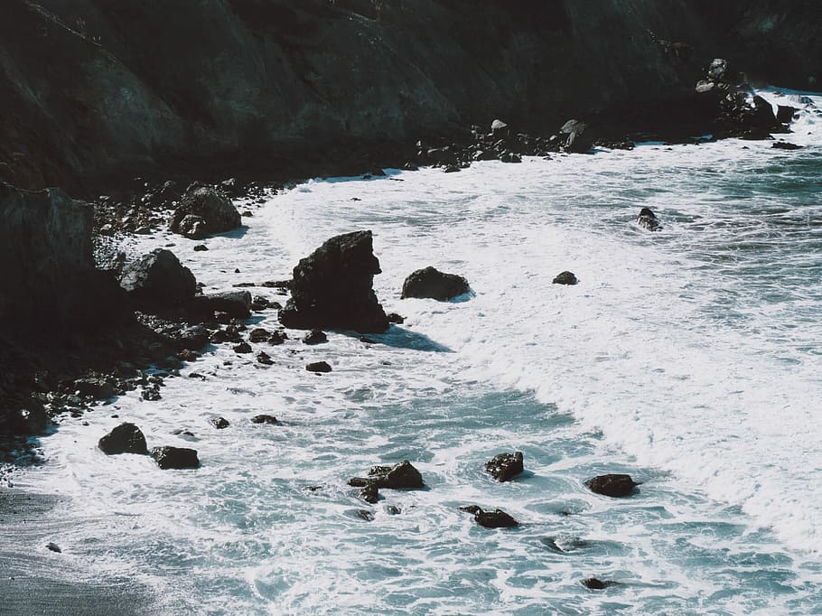 brown rock formation and body of water at daytime, waves bashing on rocky seashore at daytime