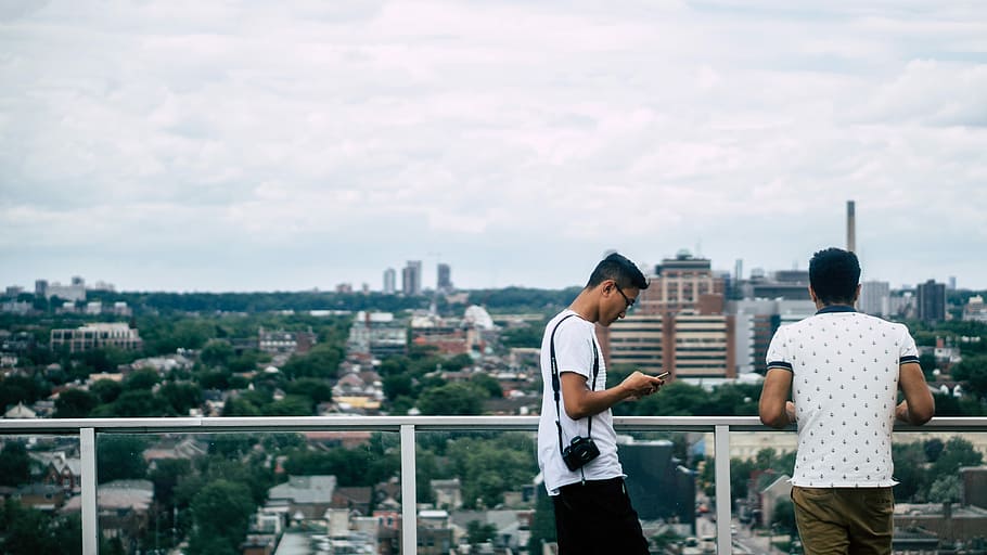 Two men are on a balcony overlooking the Toronto cityscape., two men standing in front of city buildings HD wallpaper