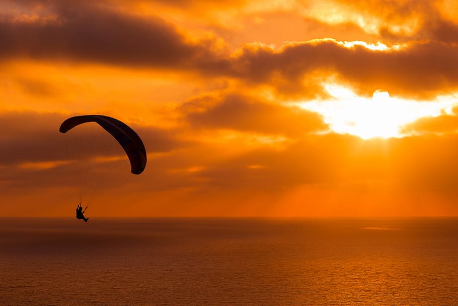 silhouette of person paragliding over ocean, person parachuting on sea during golden hour, HD wallpaper
