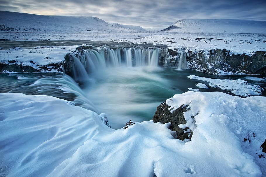 time lapse photography of waterfalls in snow, body of water surrounded by rock formation