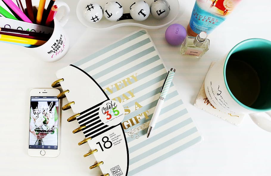 high angle photography of pen on top of book beside iPhone, mug, and fragrance bottle HD wallpaper
