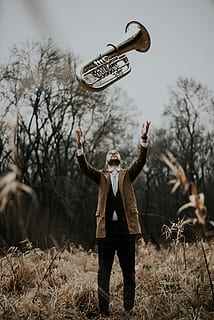 person lift musical instrument, man standing on brown grass field throwing wind instrument on air HD wallpaper