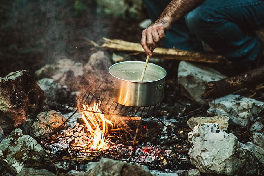 person cooking on bonefire, person holding stick while cooking on gray stainless steel pot HD wallpaper