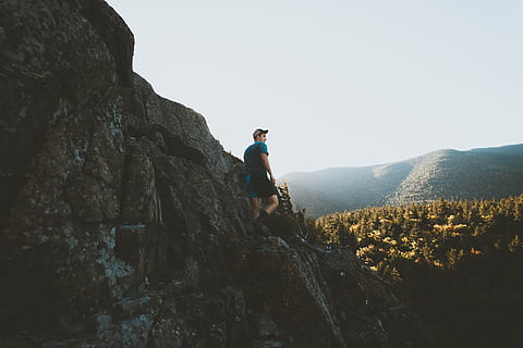 man standing on mountain cliff, man standing on rock formation near forest HD wallpaper