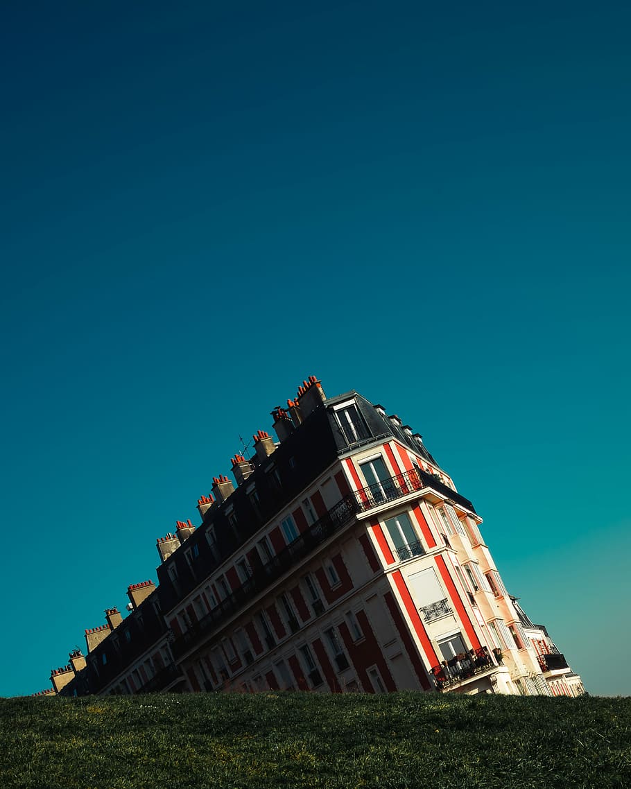 white and red concrete building under teal sky, leaning white, red, and orange building near green grass field HD wallpaper