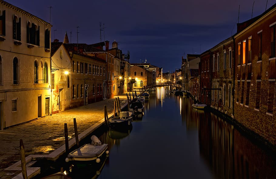 wooden dock near body of water with lights, river between brown concrete building HD wallpaper