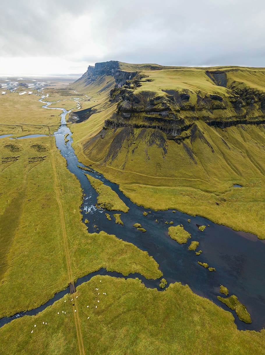 green grass covered mountain, aerial photography of green grass field with lagoon and mountain under white cloudy sky at daytime HD wallpaper