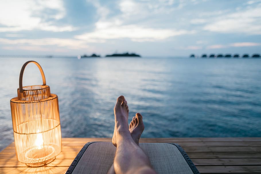 person lying on chair and facing on body of water, person with leg crossed on a dock near body of water during cloudy day HD wallpaper