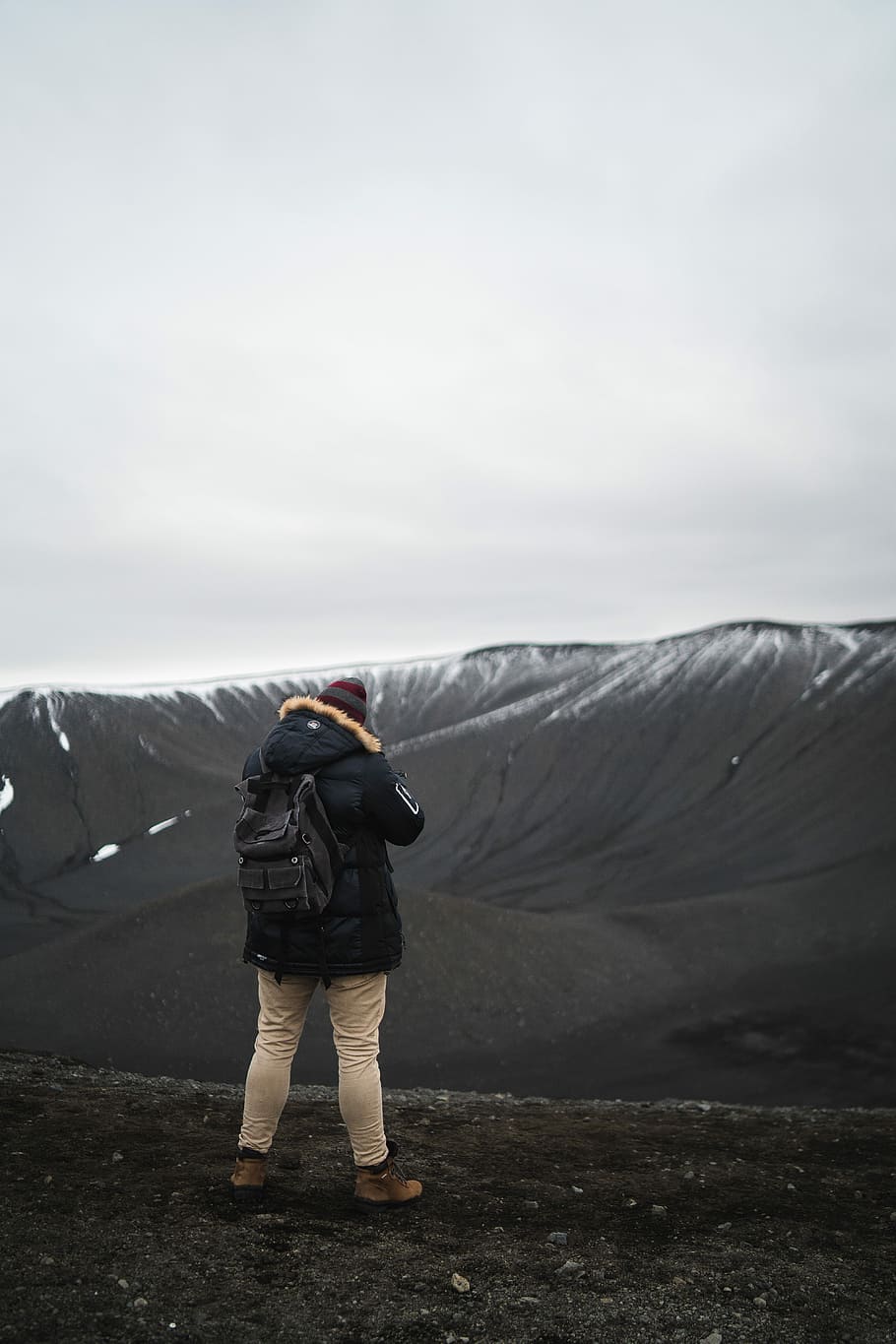 person in black parka jacket standing on brown soil, person wearing black jacket and beige pants standing on rough terrain with view of mountains photo HD wallpaper