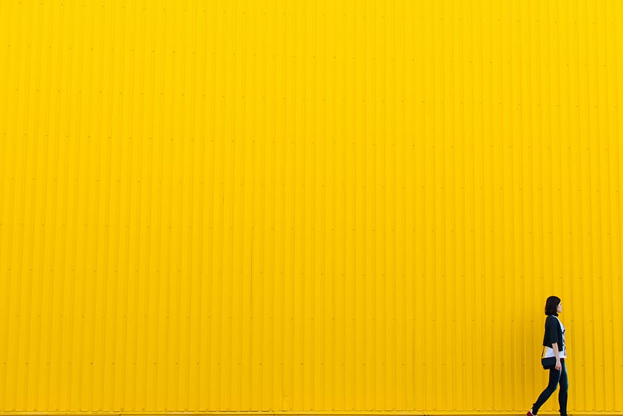 woman in black pants and cardigan walking beside yellow wall HD wallpaper