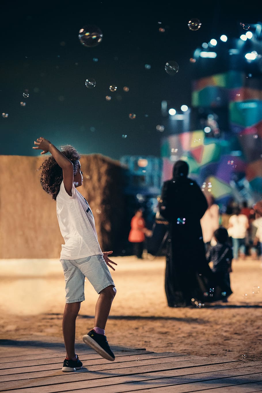 Boy with curly hair enjoying soap balloons, girl laying with bubbles during night HD wallpaper