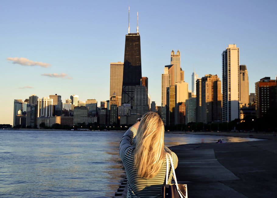 woman standing near body of water facing city buildings during daytime