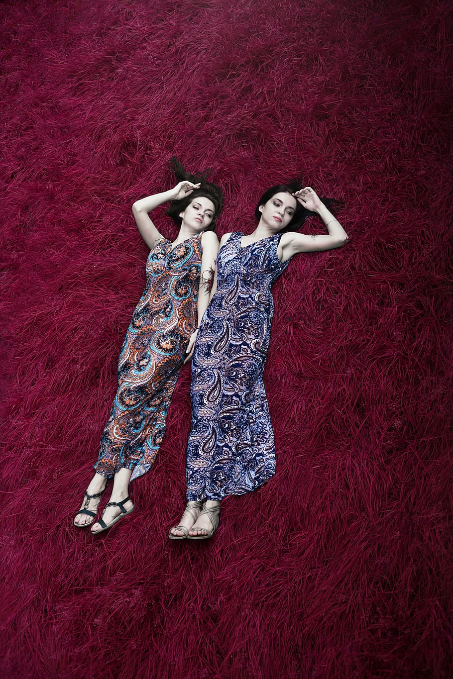two women wearing multicolored paisley-print dresses lying on red surface