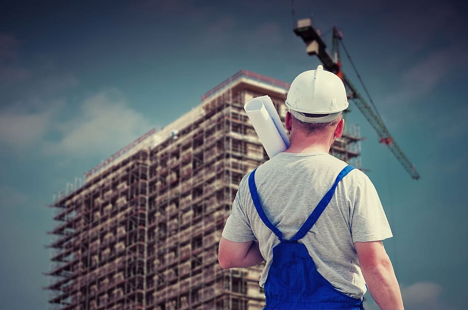 man in white hard hat, gray crew-neck t-shirt and blue jumpsuit holding paper watching building HD wallpaper