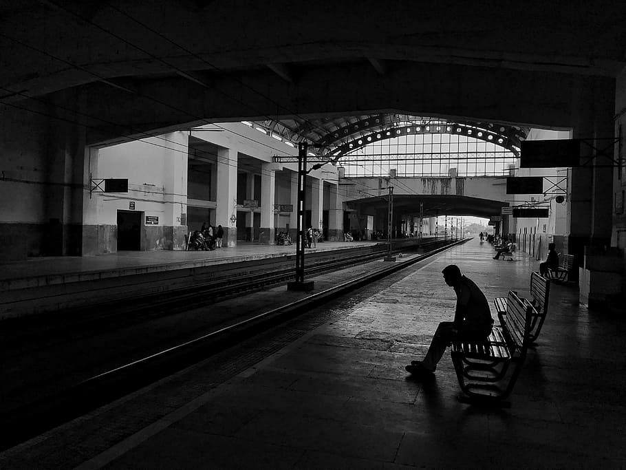 silhouette of man sitting on bench beside train rail, man sitting on bench chair under subway HD wallpaper