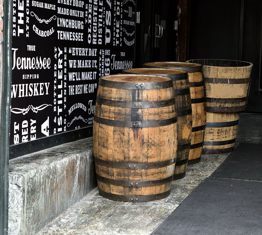 four brown beer barrel on floor beside black wall, whiskey barrels