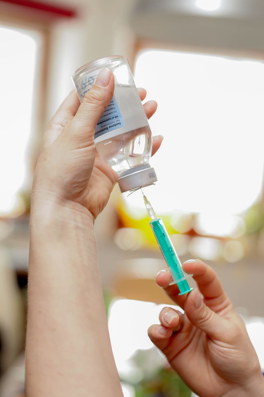 person getting clear liquid in bottle using syringe, vaccination