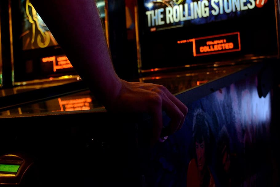 person holding The Rolling Stones machine, pinball, videogame