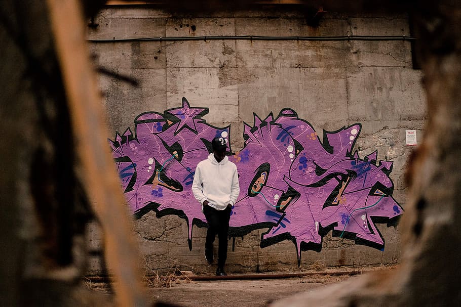 man in white pullover hoodie leaning on purple graffitied wall, man leaning on graffiti wall HD wallpaper