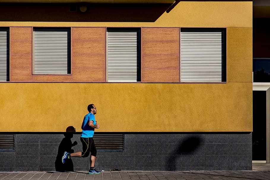 man runs on gray concrete pathway beside yellow building, exercise HD wallpaper