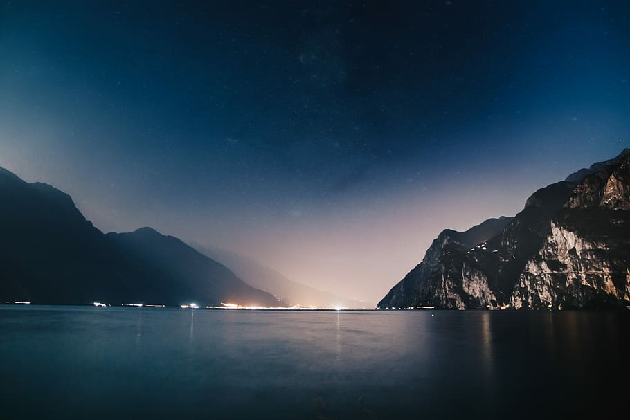 horizon scenery of mountain and sea during nighttime, city buildings near mountains and body of water HD wallpaper